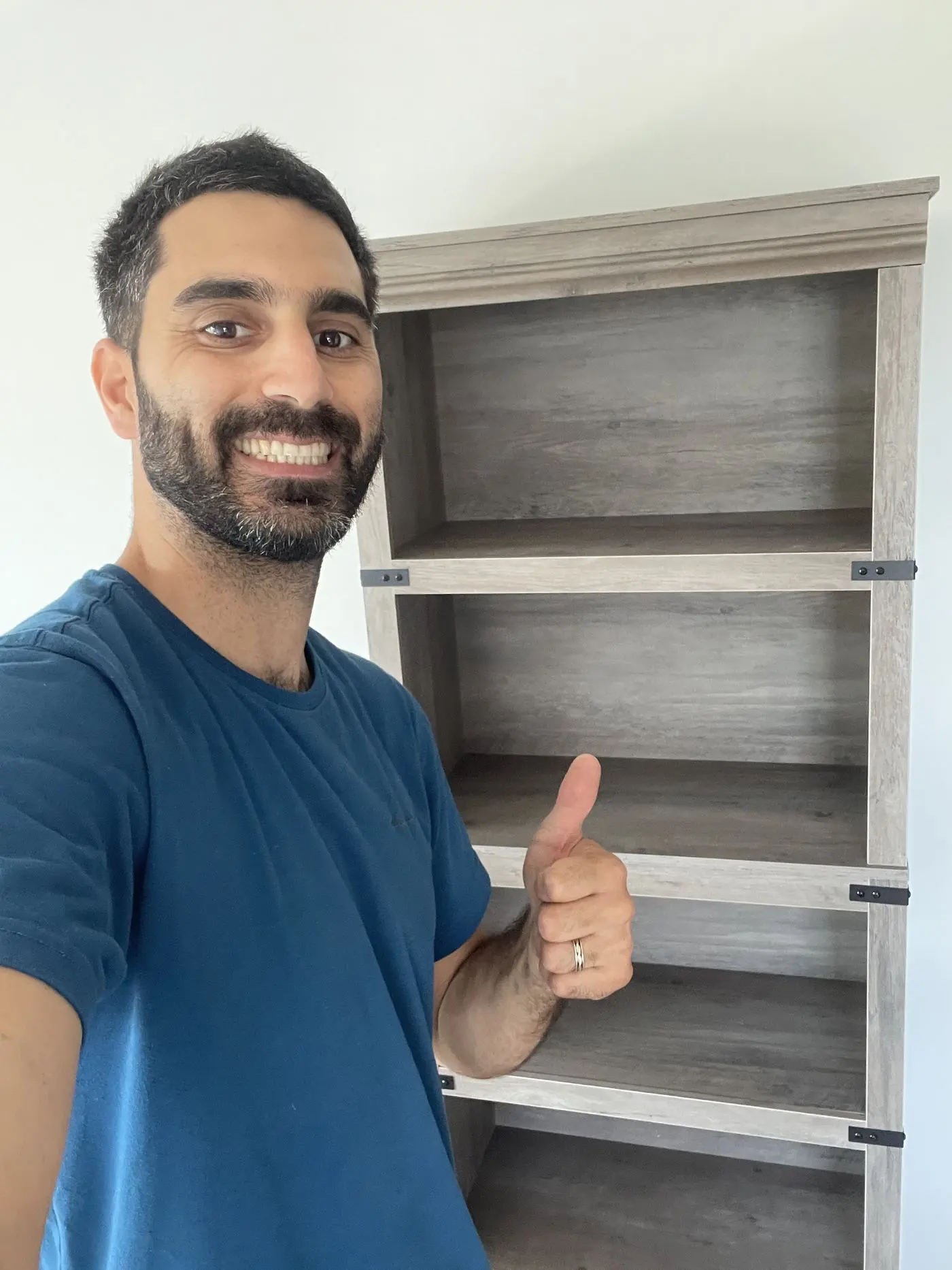 Homme souriant, le pouce levé, à côté d'une bibliothèque montée